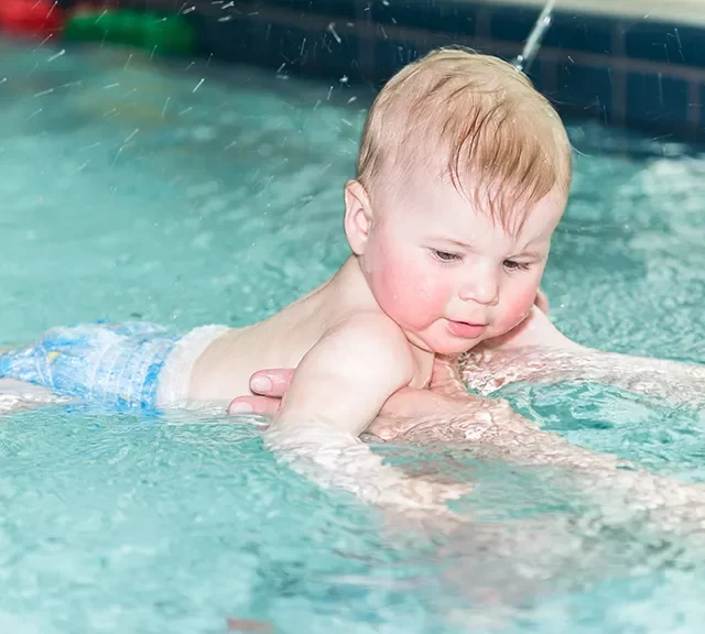 Baby wird im Wasser gehalten.